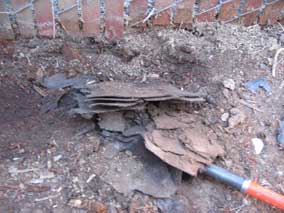 Broken roof shingles buried next to the garage where I was trying to dig a fence post hole