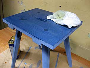 Wiping boiled linseed oil over milk paint on staked stool